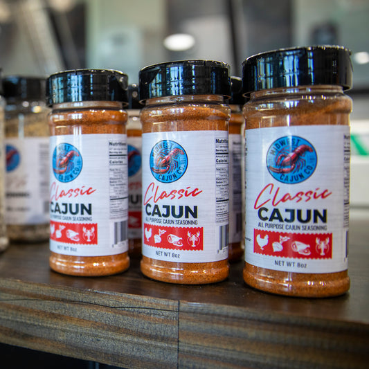 Three jars of Classic Cajun seasoning on a wooden surface with a blurred background.