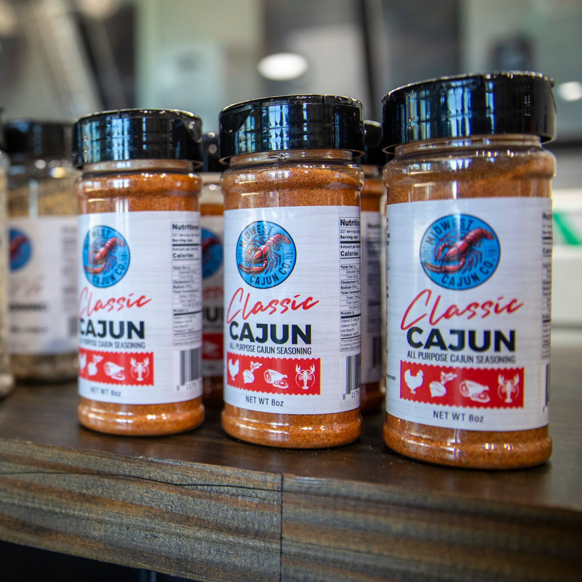Three jars of Classic Cajun seasoning on a wooden surface with a blurred background.